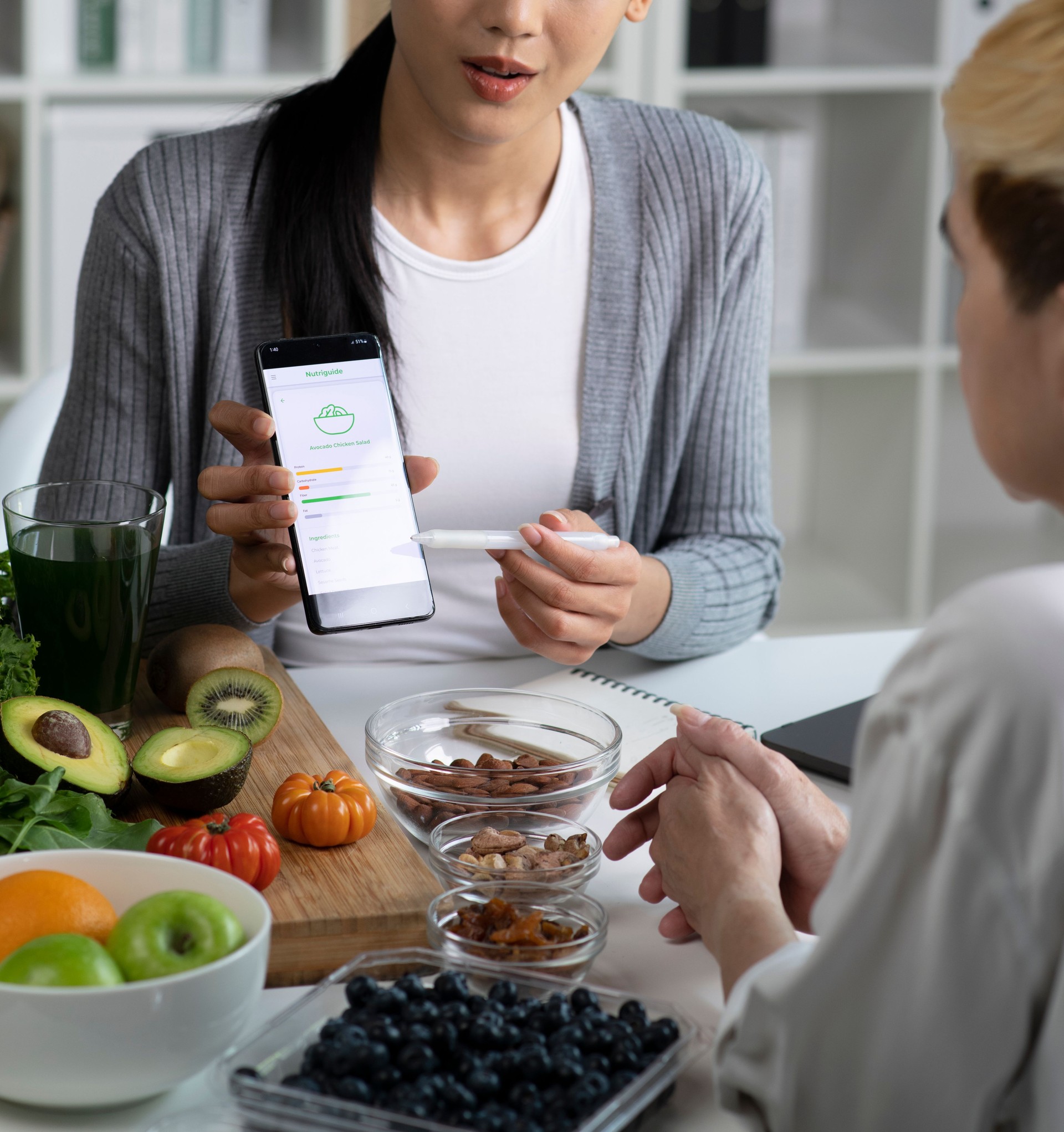 Woman Asian Professional Nutritionist explaining the data on the phone to her client, surrounded by a variety of fruits, nuts, vegetables, and dietary supplements on the table